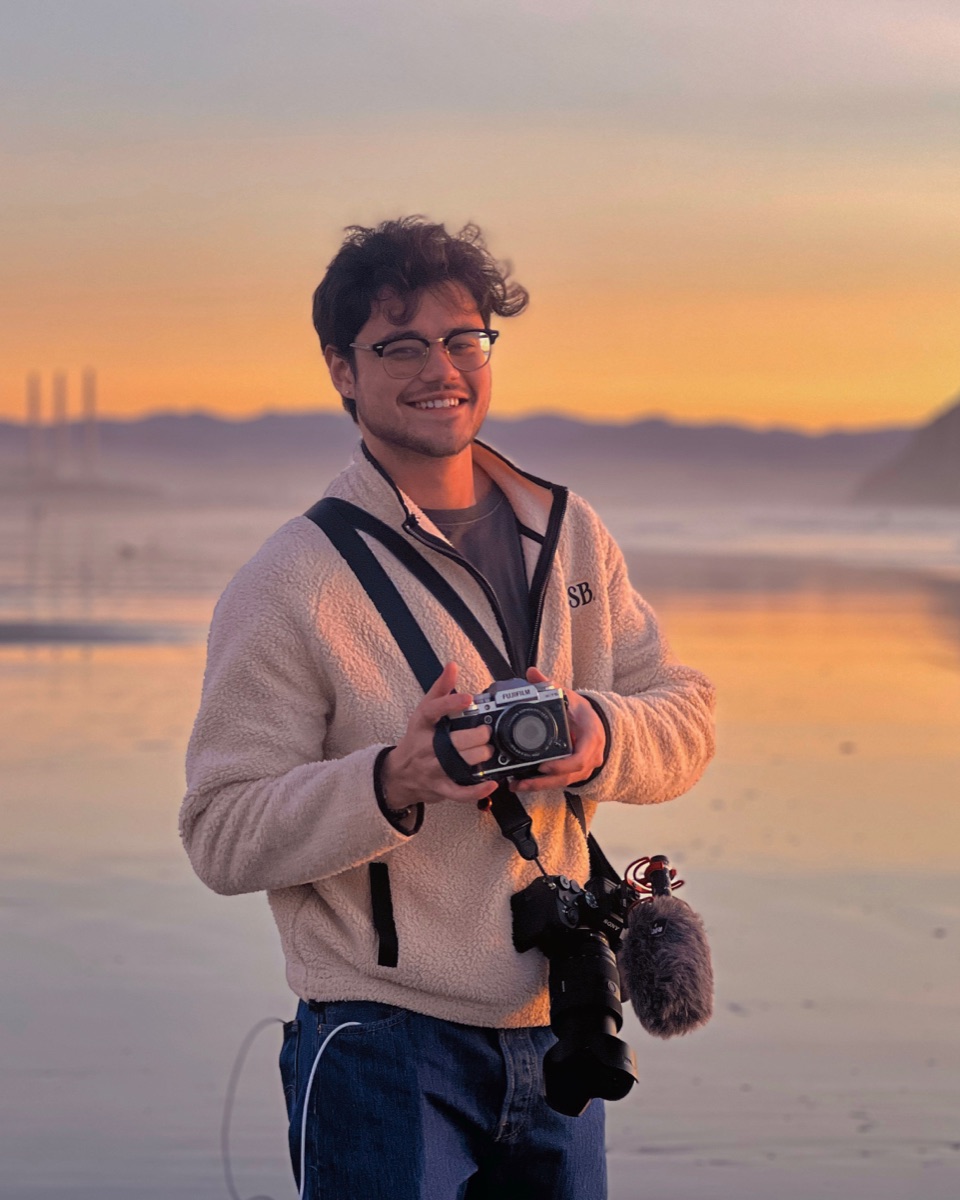 Alex Brinkley holding cameras on the beach at sunset